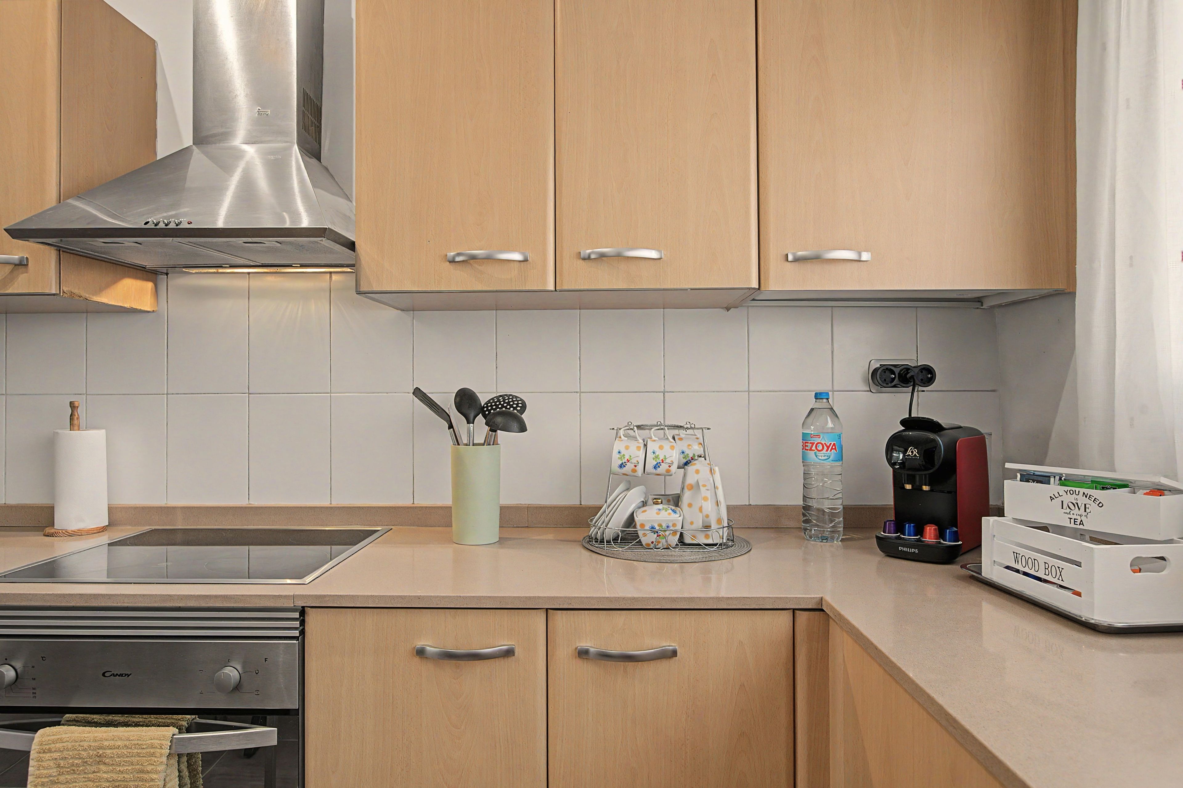 Eine moderne Küche mit Holdekor-Schränken, einer Edelstahl-Dunstabzugshaube, einem Wasserspender und einer Kaffeemaschine.