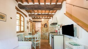 Une cuisine compacte avec un coin repas, un téléviseur fixé au mur et un mur en pierre en arrière-plan.