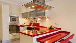 Une cuisine moderne dotée d’un îlot central, d’appareils électroménagers en acier inoxydable et de tabourets de bar rouges.