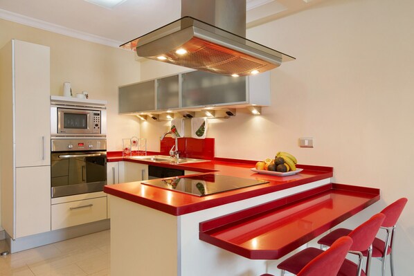A modern kitchen with a central island, stainless steel appliances, and red bar stools.