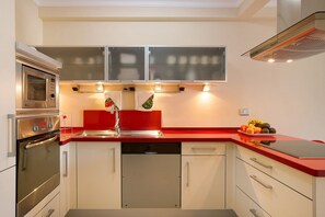 A modern kitchen with stainless steel appliances, a red countertop, and a built-in dishwasher.