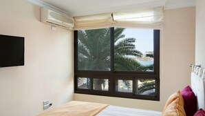 Une chambre avec un lit, une fenêtre donnant sur des palmiers et un appareil de climatisation.
