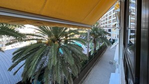 A balcony with a yellow awning, palm trees, and a view of a building with balconies. - Amazing Apartment with Sea View & Wi-Fi (Patalavaca-Mogán)