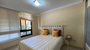 A bedroom with a bed, a window with blinds, a bedside table with a lamp, and a radiator. - Amazing Apartment with Sea View & Wi-Fi (Patalavaca-Mogán)
