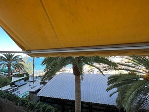 A rooftop terrace with a yellow awning, palm trees, and a view of the beach. - Amazing Apartment with Sea View & Wi-Fi (Patalavaca-Mogán)