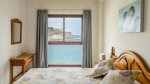 Ein Schlafzimmer mit einem Bett, einem Nachttisch, Vorhängen am Fenster und einem Gemälde an der Wand.