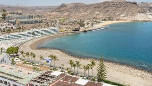 Ein Küstenhotel mit Blick auf den Strand, eine felsige Hügelkette und ein klares, blaues Meer.