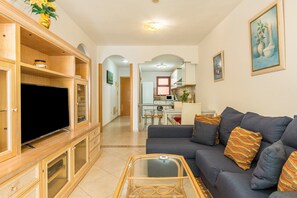 A living room with a TV, sofa, and a dining area in the background.