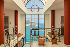 A spacious interior with a view of the sea, a staircase, and potted plants.