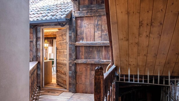 Un interior de madera con techo de baldosas, una escalera de madera y una puerta que da a otra habitación.