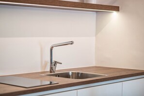 Une cuisine moderne dotée d’un évier en acier inoxydable, d’un plan de travail en bois et d’un éclairage intégré au-dessus de l’évier.
