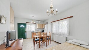 A room with a bed, a desk with a computer, a dining table with chairs, a kitchen area, and a chandelier.