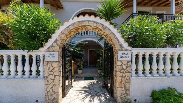 A stone archway leading to a villa entrance, flanked by white balustrades and lush greenery.