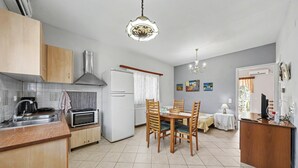 A kitchen with a sink, stove, and microwave, a dining area with a table and chairs, and a living area with a TV and lamp.
