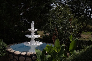 Una fuente blanca escalonada en un jardín con borde de piedra y abundante vegetación.