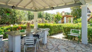A covered patio with a stone floor, a central table with chairs, and a bench.