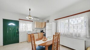 A kitchen with a dining table, chairs, a refrigerator, and a window with lace curtains.