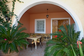 An outdoor patio with a table and chairs, surrounded by potted plants and a stone wall.