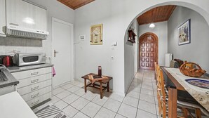 Una cocina con microondas, armarios, una mesita y un comedor con sillas y mantel.