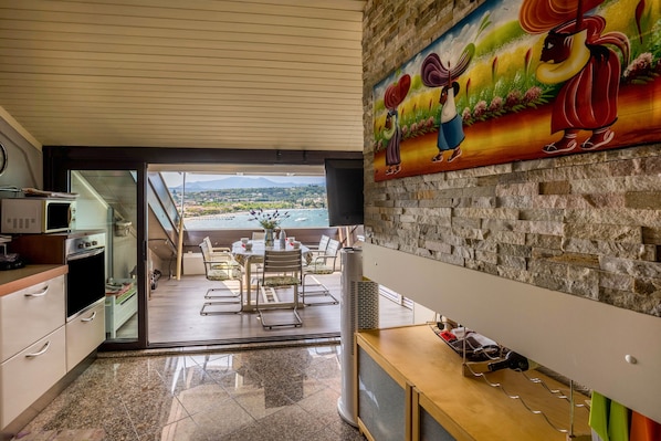 A modern kitchen with a view of a body of water, a dining area with outdoor seating, and a stone wall with a colorful mural. - Apartment 'Residence Gigi Complex' with Lake View, Terrace and Wi-Fi (Manerba del Garda)