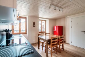 Una cocina compacta con armarios de madera, un refrigerador rojo, una mesa de comedor con sillas y una ventana que proporciona luz natural.