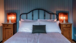 Un lit avec du linge de lit blanc et un oreiller foncé, flanqué de deux tables de chevet en bois sur lesquelles sont posées des lampes.