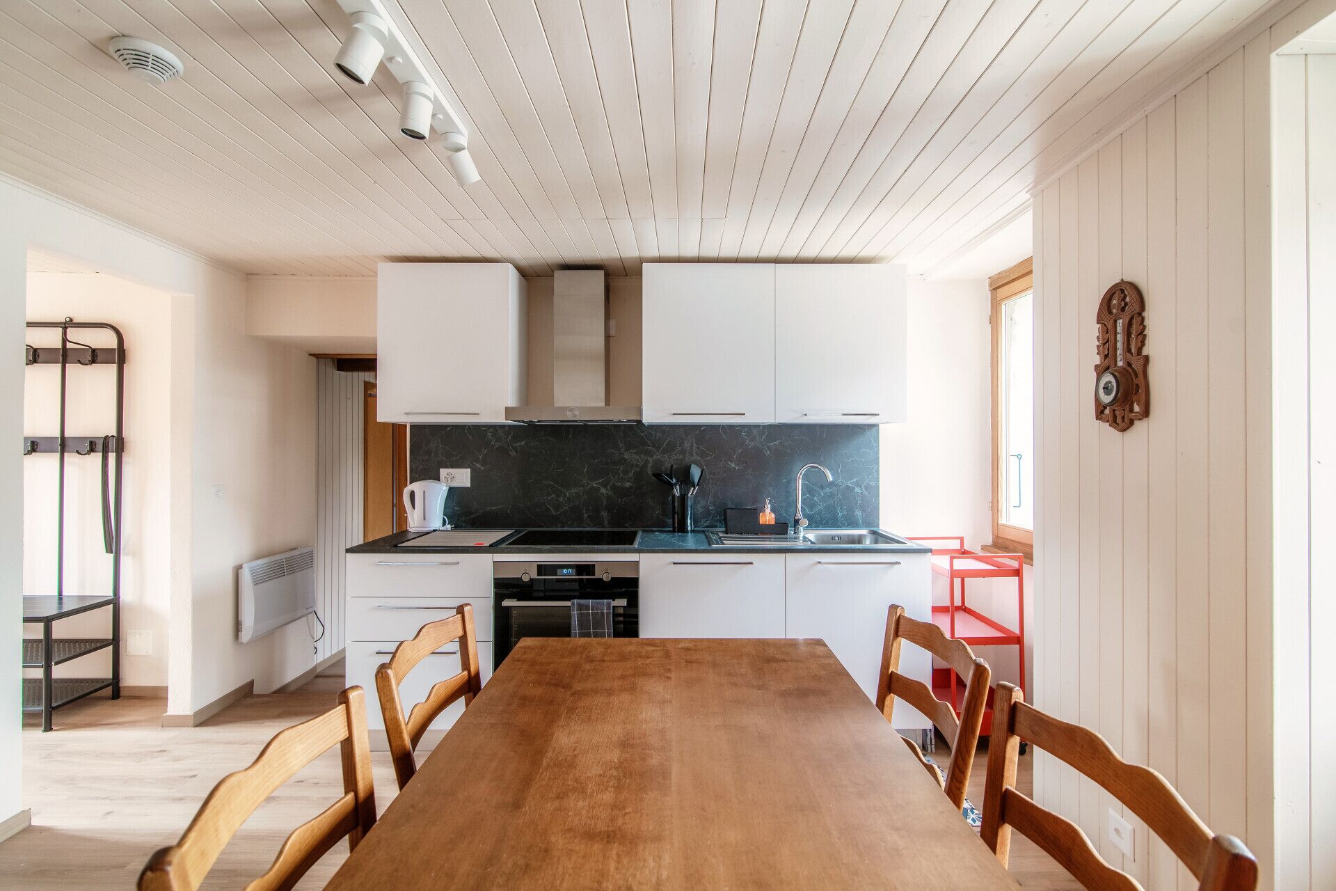 Une cuisine moderne avec des meubles blancs, un plan de travail noir et une table à manger en bois, accompagnée de chaises.