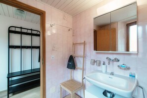 Un baño con lavamanos blanco, un espejo, una silla de madera y un estante de metal negro.