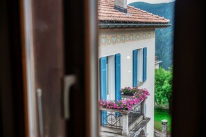 A view through an open door of a building with blue shutters, a tiled roof, and a balcony with pink flowers.