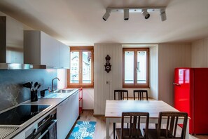 Une cuisine compacte équipée d’une cuisinière, d’un évier et d’un réfrigérateur rouge. On y trouve une table à manger avec des chaises, ainsi qu’une fenêtre qui laisse entrer la lumière naturelle.
