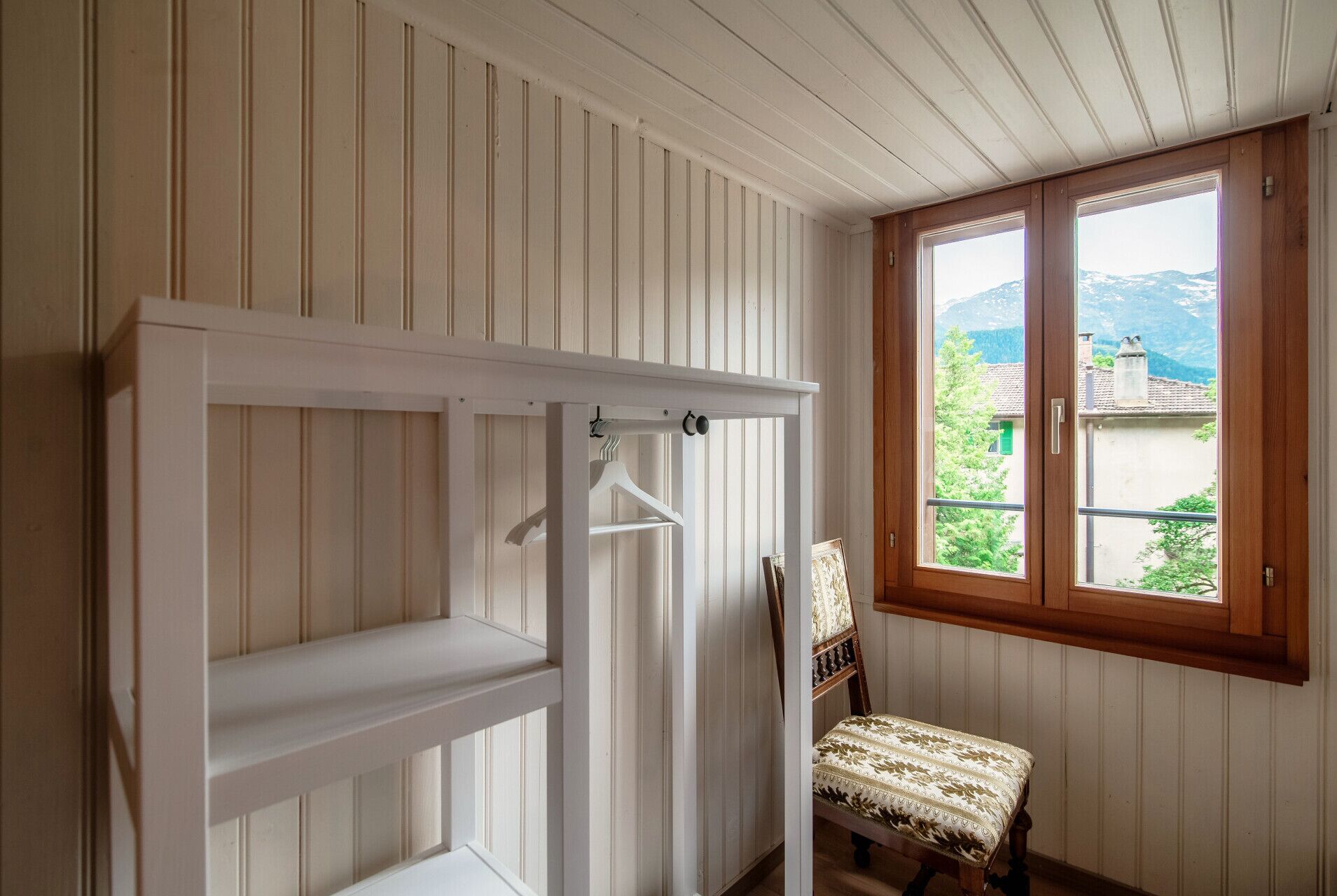 Een kamer met een houten bankje, een witte deurpost en een raam met uitzicht op een berg.