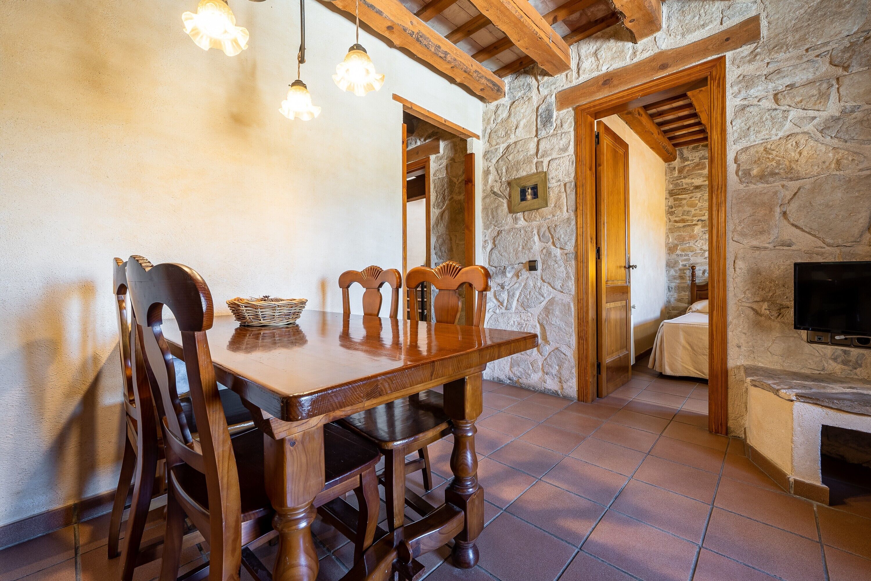 Un comedor con una mesa y sillas de madera, una pared de piedra y un televisor.