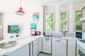 A modern kitchen with white cabinets, a red pendant light, a sink, a microwave, and a window with a view of greenery.