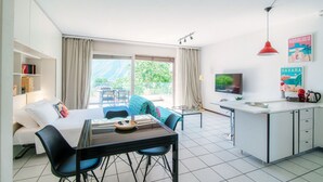A modern hotel room with a bed, a dining area, a kitchen, and a balcony with a view. - Open-space apartment with lake view (PANORAMIC STUDIO) (Lugano)