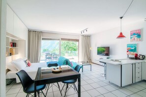 A modern hotel room with a bed, a dining area, a kitchen, and a balcony with a view. - Open-space apartment with lake view (PANORAMIC STUDIO) (Lugano)