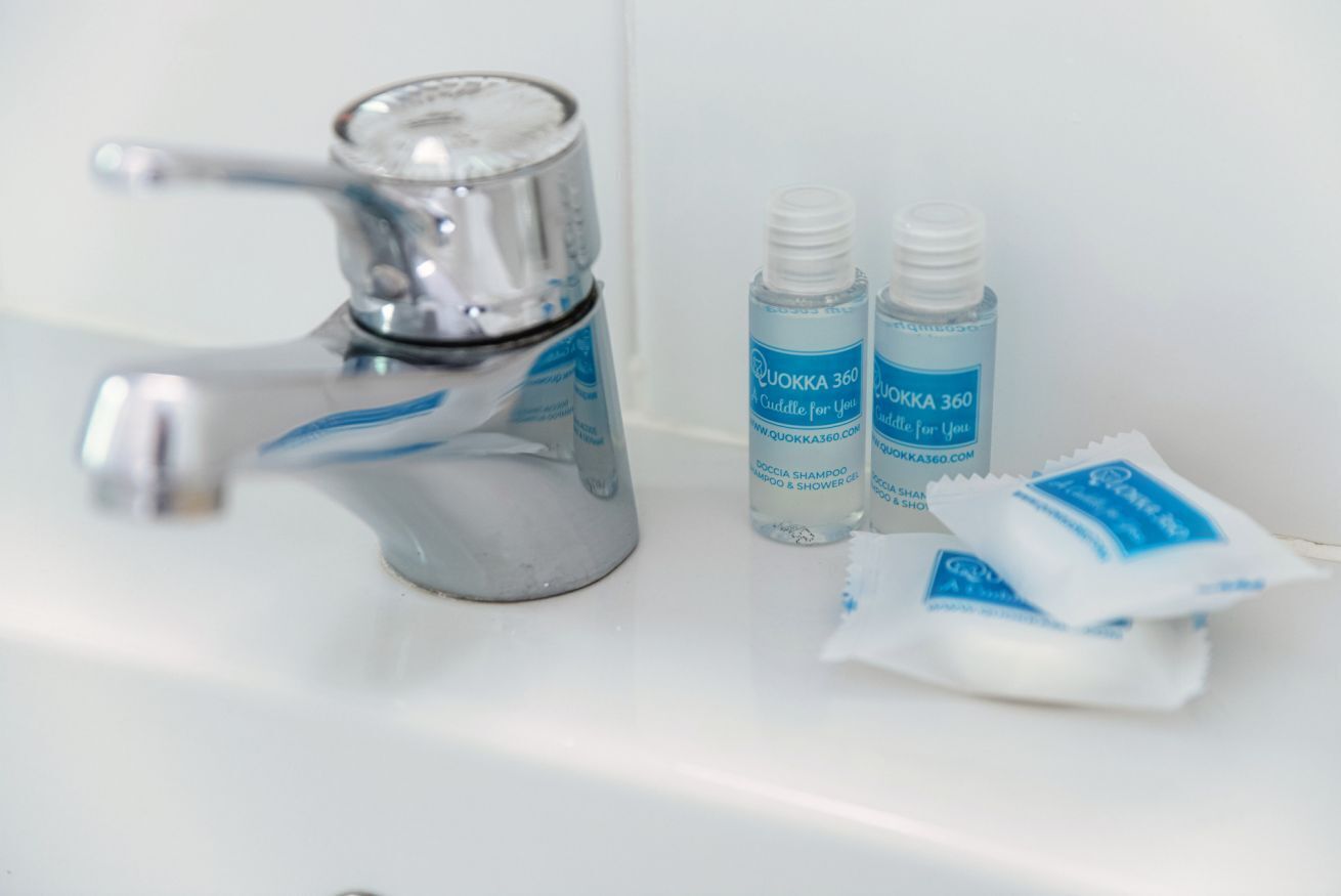 Un lavabo de salle de bain avec un robinet, deux bouteilles de shampoing Quokka 360 et un sachet de shampoing.