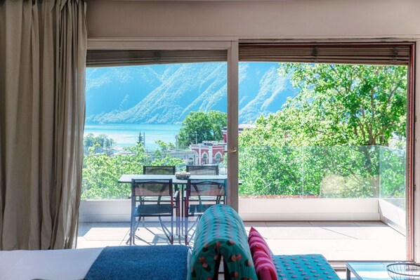 A hotel room with a large window offering a view of a lake and mountains.