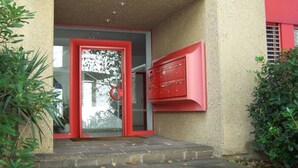 A building entrance with a glass door and a red mailbox. - Open-space apartment with lake view (PANORAMIC STUDIO) (Lugano)