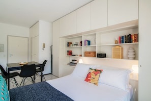 Ein Hotelzimmer mit einem Bett, einem Schreibtisch mit Stühlen und einem Bücherregal mit Büchern und Dekoration.