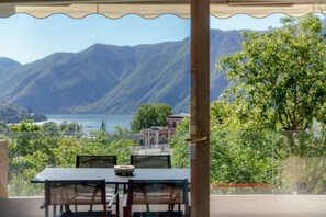 A terrace with a table and chairs, overlooking a mountainous landscape and a body of water.