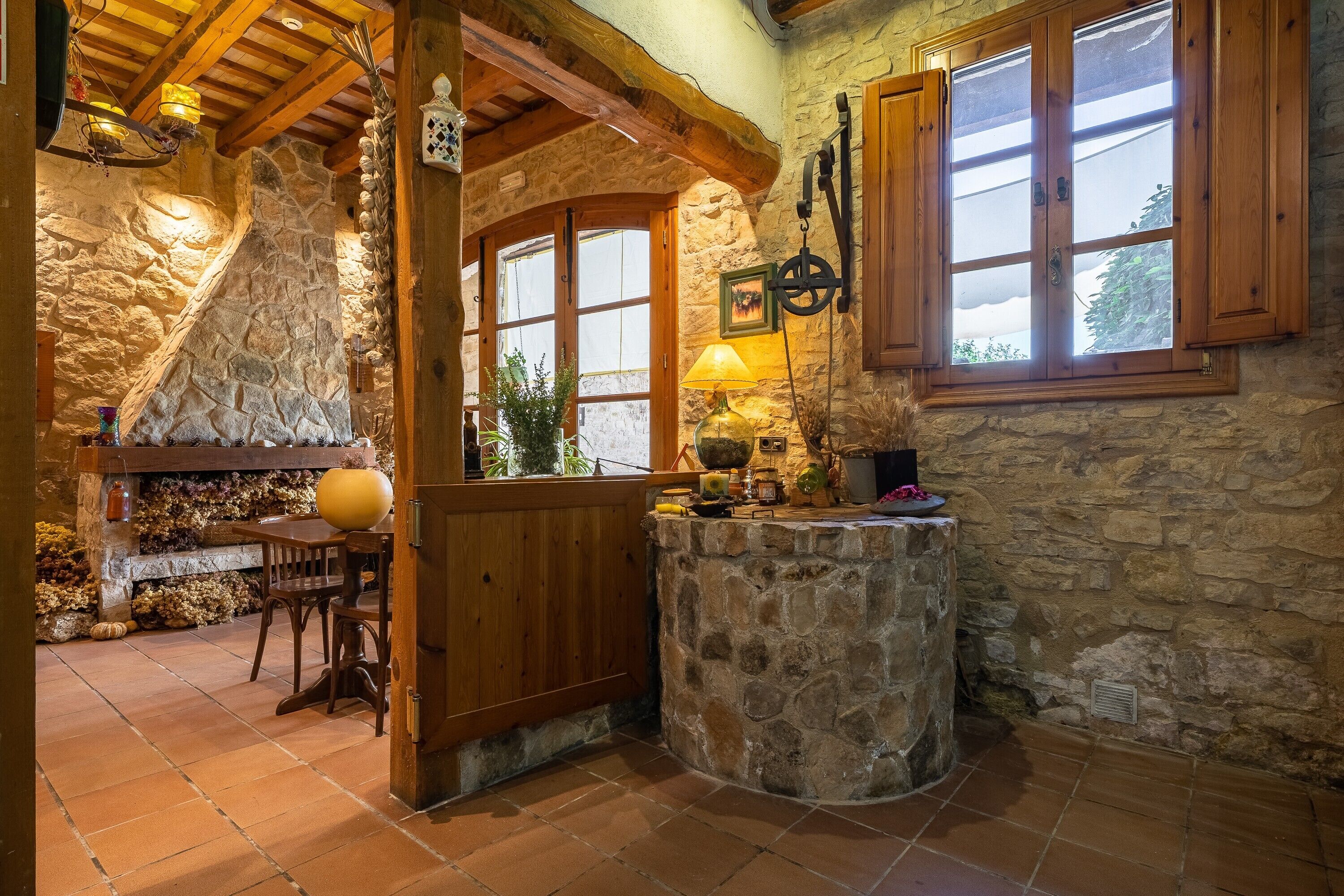 A rustic stone interior with wooden beams, a stone fireplace, and a wooden counter with a lamp.