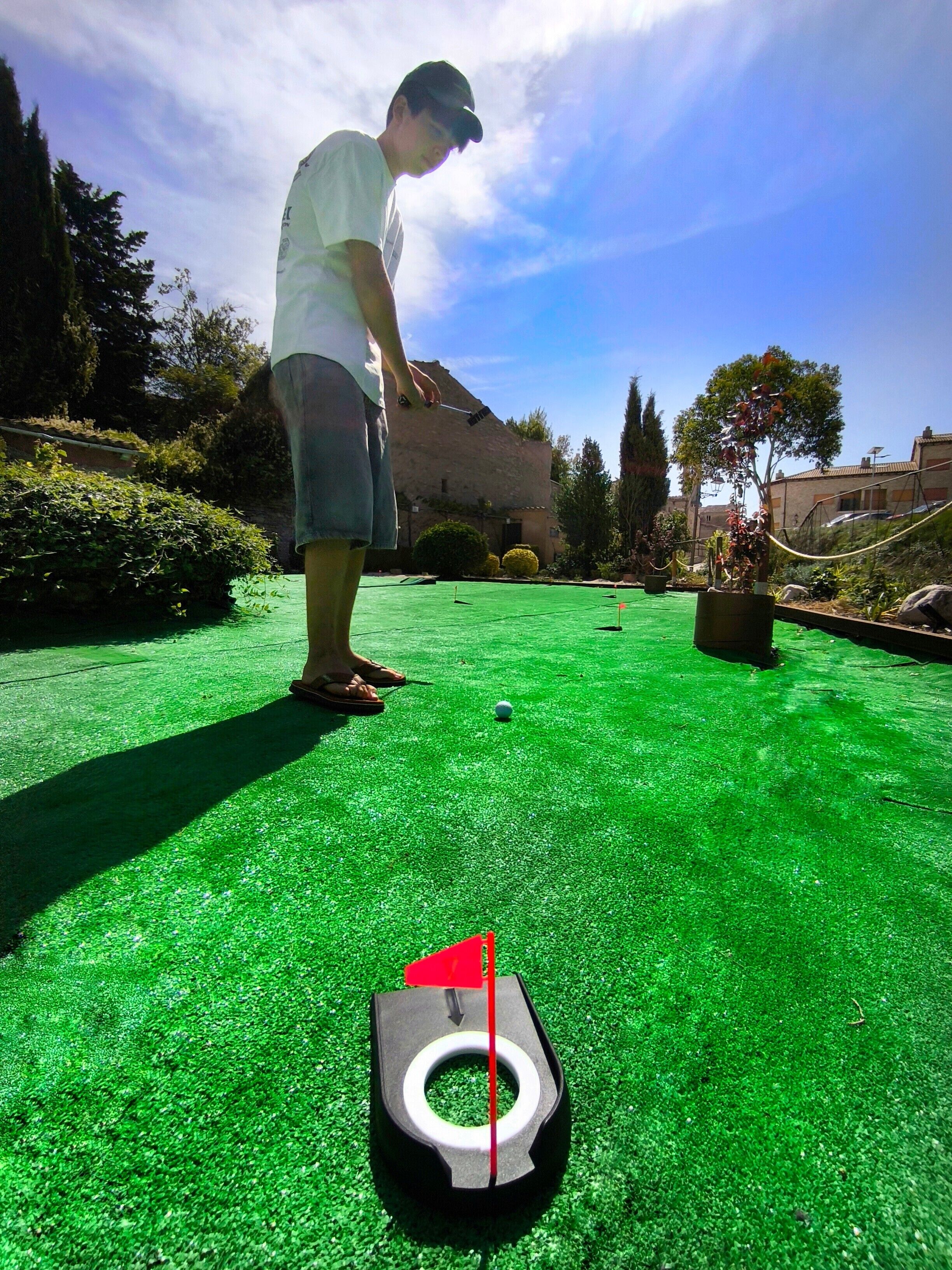 A person playing golf on a green field with a hole marked by a flag.