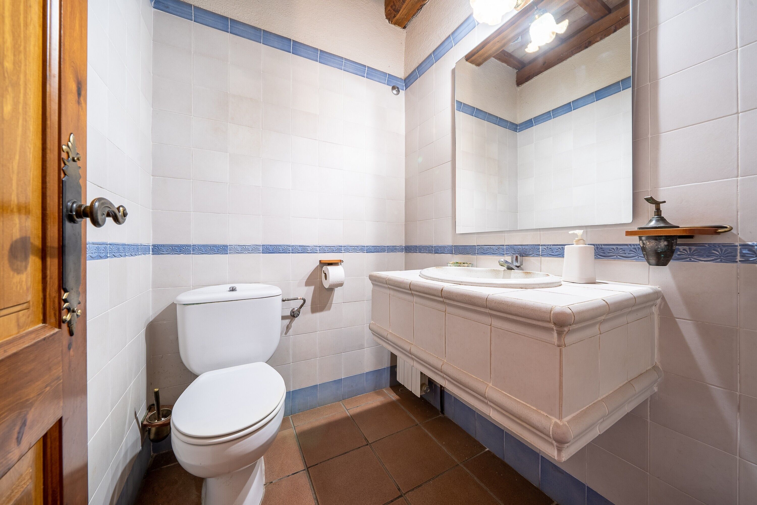 Un baño con inodoro, lavabo, espejo y paredes con azulejos azules.