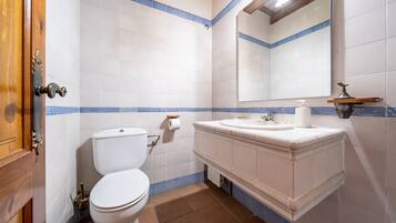 Un baño con inodoro, lavabo, espejo y paredes con azulejos azules.