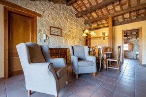 Un interior rústico con paredes de piedra, vigas de madera y una zona de comedor con mesa y sillas de madera.