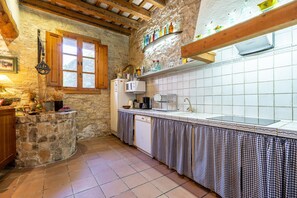 Una cocina rústica con paredes de piedra, vigas de madera, salpicadero de azulejos y un mantel a cuadros cubriendo la encimera.