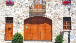 A stone building with a large wooden double door, two windows with flower boxes, and a small balcony with a railing. - Apartment 'El Clos 3' with Mountain Views, Private Terrace and Wi-Fi (CONESA)