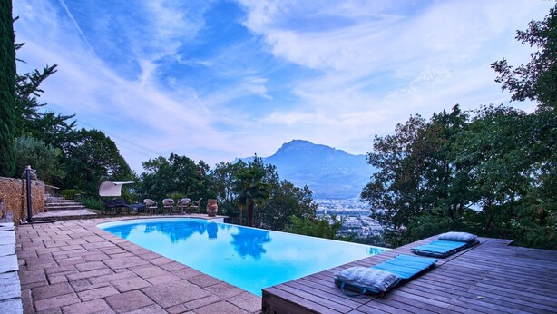 Une piscine avec une terrasse en bois, des sièges extérieurs et une vue sur la montagne.
