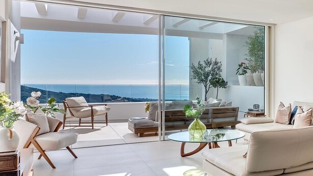 A modern living room with a glass sliding door leading to a balcony with a sea view. - Palo Alto Marbella Luxury Apartment – Sea View, Wi-Fi & Air Conditioning (Ojén)