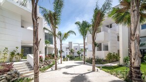 A modern building with a courtyard, palm trees, and a stone wall. - Palo Alto Marbella Luxury Apartment – Sea View, Wi-Fi & Air Conditioning (Ojén)